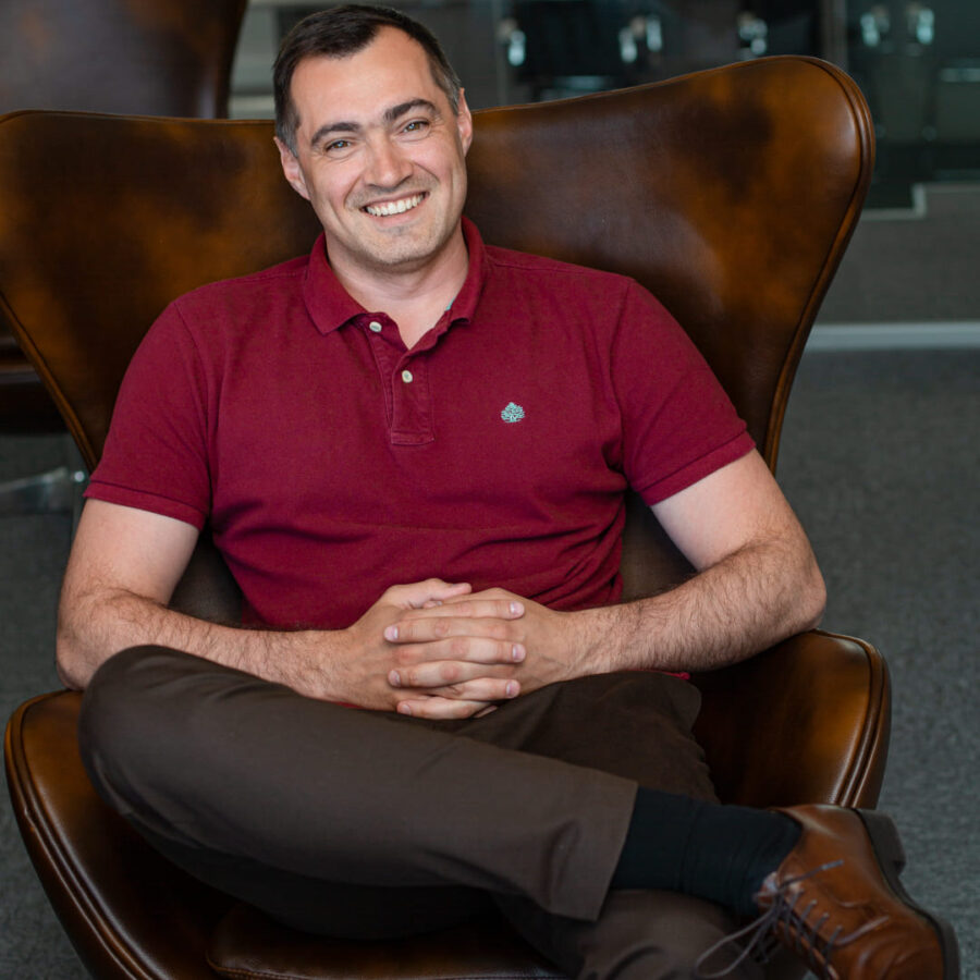 Professional portrait showcasing a relaxed and approachable business leader seated in a modern office environment, exuding confidence and warmth.